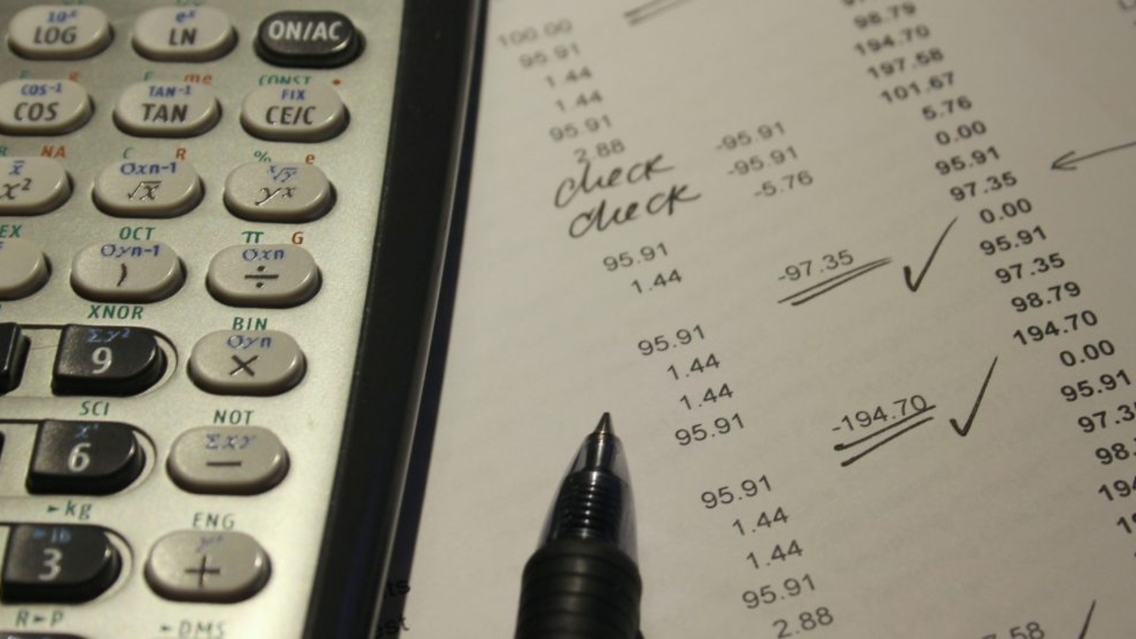 Kalkulators pa kreisi, papirs ar cipariem un pildspalva